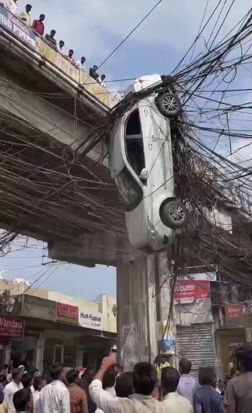 A car was left dangerously suspended in a massive web of overhead electrical wires beneath a flyover. The unusual incident shocked onlookers as people gathered to see how the vehicle ended up tangled